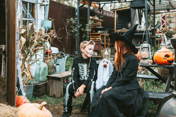 children a boy in a skeleton costume and a teenage girl in a witch costume having fun at a Halloween party on the decorated porch suburban house