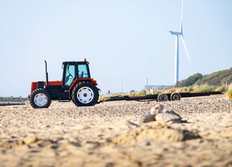 read tractor with boat trailer on the sandy beach with a wind turbine in the background