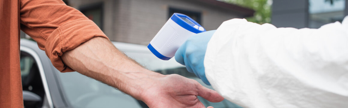 Cropped view of medical worker holding pyrometer near man and blurred car, banner