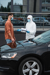 Naklejka premium Driver in mask standing near medical worker with clipboard pointing with hand outdoors