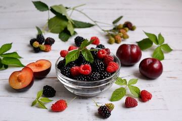 The concept of a juicy and vitamin summer. Ripe raspberries, blackberries, plums and mint leaves on a light background, close-up