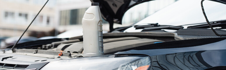 Bottle of motor oil on car with open hood, banner