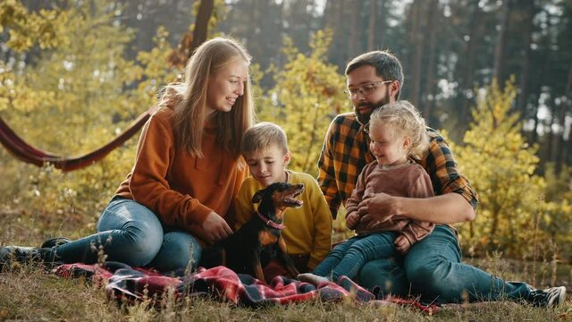 Beautiful family with little children and a dog relaxing together while sitting on a plaid in an autumn park
