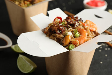 Box of wok noodles with seafood on black table, closeup