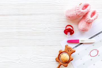 Pregnancy test with pink baby girl booties and calendar, top view