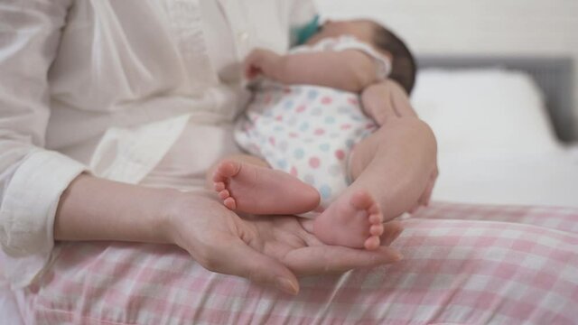 selective focus shot a pair of cute little feet of the newborn infant who’s sleeping peacefully in her mother’s arms.