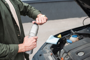 Cropped view of driver opening bottle of motor oil near car outdoors