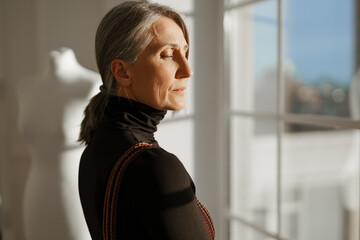 European senior woman with grey hair posing by window and dummy