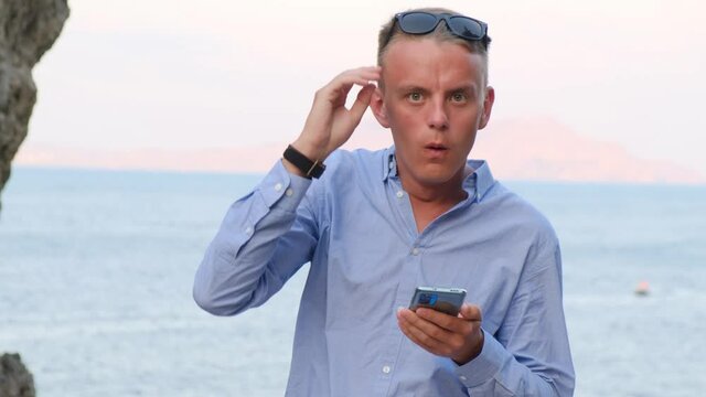 Surprised man looking at smartphone screen against the background of the sea and mountains