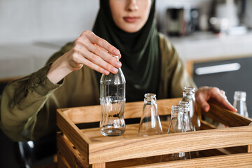 Young muslim woman wearing hijab separating waste while sitting at table