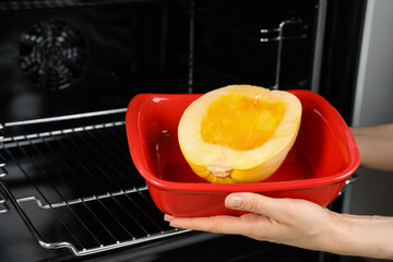 Woman putting half of fresh spaghetti squash into oven, closeup