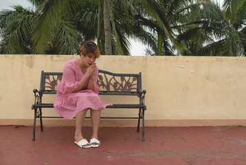 An asian lady in her 20s prays while sitting on a bench outdoors. Hoping for good results.