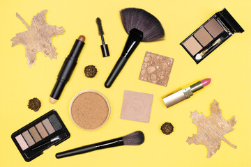 Autumn make-up flat lay. Makeup products brown, bronze, gold colors with fall decorations on yellow background. Top view