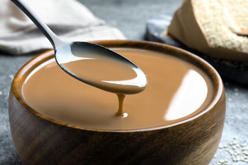 Spoon of tasty sesame paste above bowl, closeup