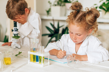 Little boy and girl in white uniforms look into the microscope in a laboratory.Back to school concept.Young scientists.Natural sciences.Preschool and school education of children.