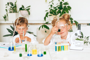 Serious little boy and girl in white uniforms conducting chemical experiments in a laboratory.Back to school concept.Young scientists.Natural sciences.Preschool and school education of children.