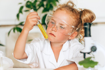 Serious little red-haired girl in white uniform conducting chemical experiments in a...
