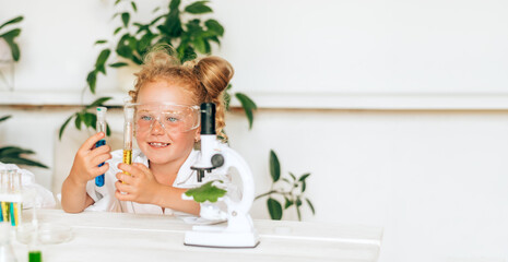 Positive little red-haired girl in white uniform conducting chemical experiments in a...
