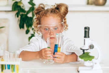 Surprised little red-haired girl in white uniform conducting chemical experiments in a laboratory.Back to school concept.Young scientists.Natural sciences.Preschool and school education of children.
