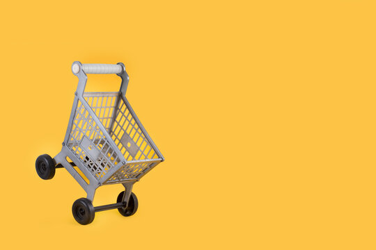 Carro de supermercado vac&iacute;o sobre un fondo amarillo liso y aislado. Vista de frente. Copy space