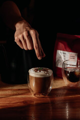 a hand of barista making and decoring a glass of coffee with milk foam