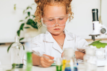 Little red-haired girl in white uniform conducting chemical experiments in a laboratory.Back to school concept.Young scientists.Natural sciences.Preschool and school education of children.