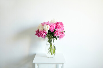 Empty white wall with pink flowers. Peonies in a glass vase in a bright interior