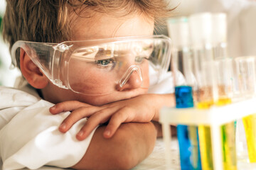 Serious little boy in white uniform conducts chemical experiments in a laboratory.Back to school concept.Young scientists.Natural sciences.Preschool and school education of children.