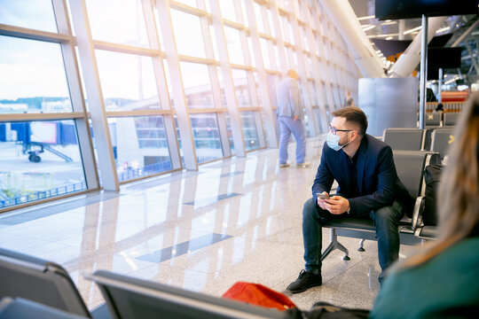 Traveler business man with face mask use smart phone online stock in airport terminal. Concept cryptocurrency trading, communication social networks.