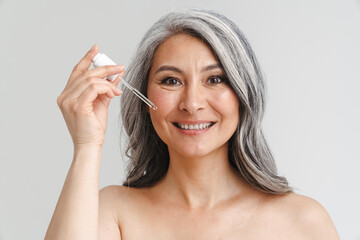 Mature shirtless woman with grey hair applying face serum