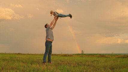 Dad throws his happy son into sky in park in front of a rainbow. Father, child play, laugh and rejoice together. Happy family trip. The baby is in arms of a parent. Dad is off. Happy family concept