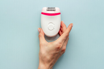 Female hand with white epilator for hair removal. Depilatory overhead view