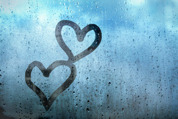 Two hearts drawn by finger on fogged window glass with raindrops