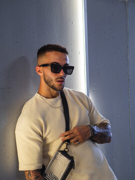 Hombre joven con tatuajes posando en una pared con neones 