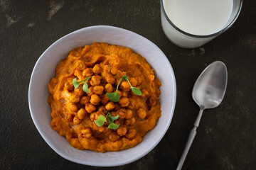 Thick pumpkin soup with baked chickpeas and radish sprouts in a plate with a glass of milk on the table, delicious healthy dinner