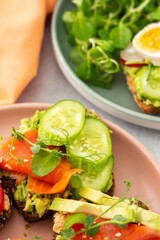 Healthy tasty breakfast, sandwiches with avocado and salmon, cucumbers and tomatoes, radishes and microgreens of peas with boiled egg and root salad