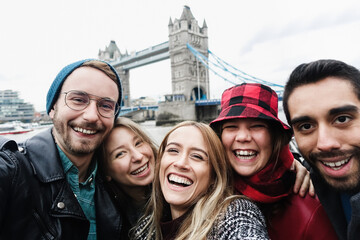 Happy friends having fun taking selfie with mobile phone in London with Tower Bridge in background - Travel concept - Focus on center girl face