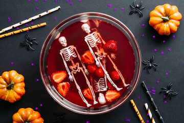 Halloween party concept. Bowl with blood, strawberries, skeletons and halloween decorations on black background. Flat lay, top view.