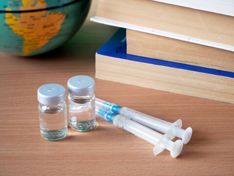bottles and syringes of vaccine aganist covid-19 near book pile and school supplies, back to school in coronavrus time concept