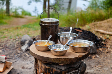 Lunch break at camp. Cooking simple delicious soup on fire, serving in touristic metal bowls. Concept of food preparation in travelling, camping, trekking, hiking trips. Bowler pot on background