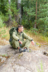 Fototapeta premium Young man travelling alone with a backpack. Concept of active tourism, camping in the forecast, trekking and hiking during vacations. Green background. Copy space for text