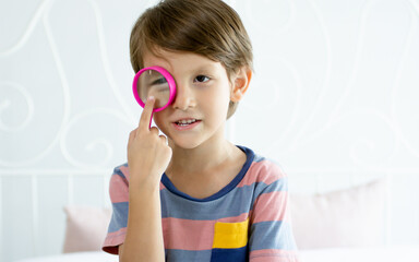 Little adorable Caucasian boy wearing casual cloth, standing, holding and playing magnifying glass as toy to investigate, supposing to be scientist or researcher as his dream. Kid, Education Concept.