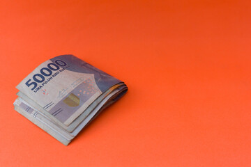 The pile of Indonesian currency is rupiah which is fifty thousand rupiah. Indonesian currency isolated orange. For illustrations of economic news, buying and selling, taxes, savings, corruption