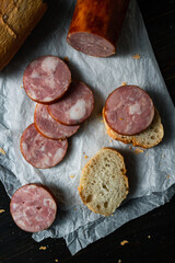 Slices of round sausage on slices of baguette on parchment paper wand wooden table