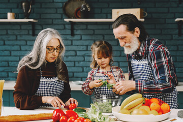 Senior grandparents couple with dgranddaughter cooking in kitchen