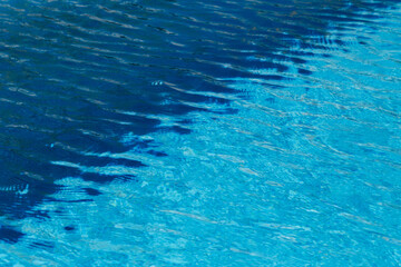 Two colored light and dark blue water with ripples and sunny reflections in swimming pool.