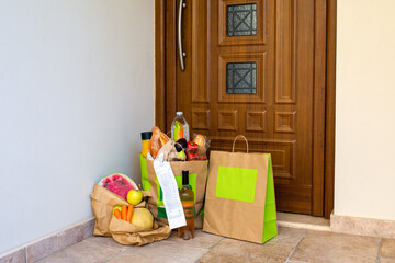 A grocery bag under the door of the house.Food delivery to the door in craft bags.Home delivery of organic products.Packaged vegetarian food.Safe food delivery during a pandemic.Delivery of groceries 
