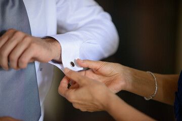 Mani femminili che sistemano il polsino con i gemelli della camicia bianca indossata dallo sposo