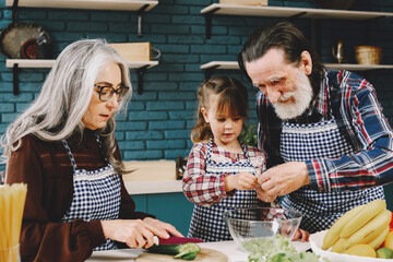 Senior grandparents couple with dgranddaughter cooking in kitchen