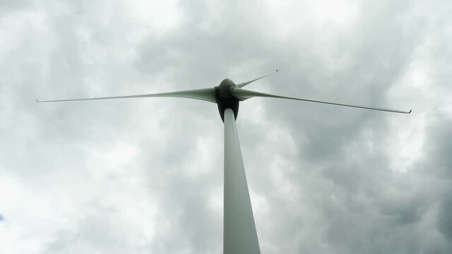 Bottom view of working wind turbine power generator against dark cloudy sky